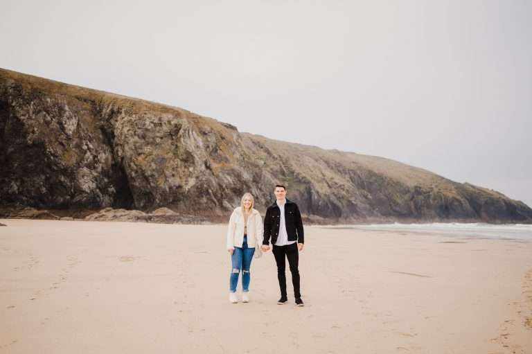 Standing side by side the newly engaged couple stand with Holywell Bay in The background