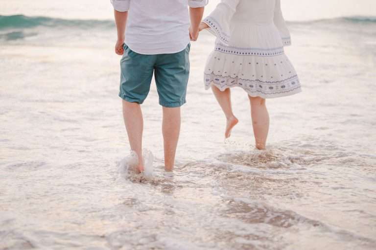 Couple enjoying celebrating their engagement whilst walking through the sea - What To Do Now You're Engaged