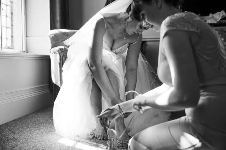 Black and white of the bride doing up her wedding shoe in the light of the window at The Alverton