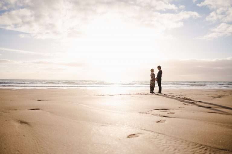 As The sun goes down it leaves a golden glow behind the happy couple holding hands on the beach in Cornwall - Engagement Shoot - The Ultimate Guide