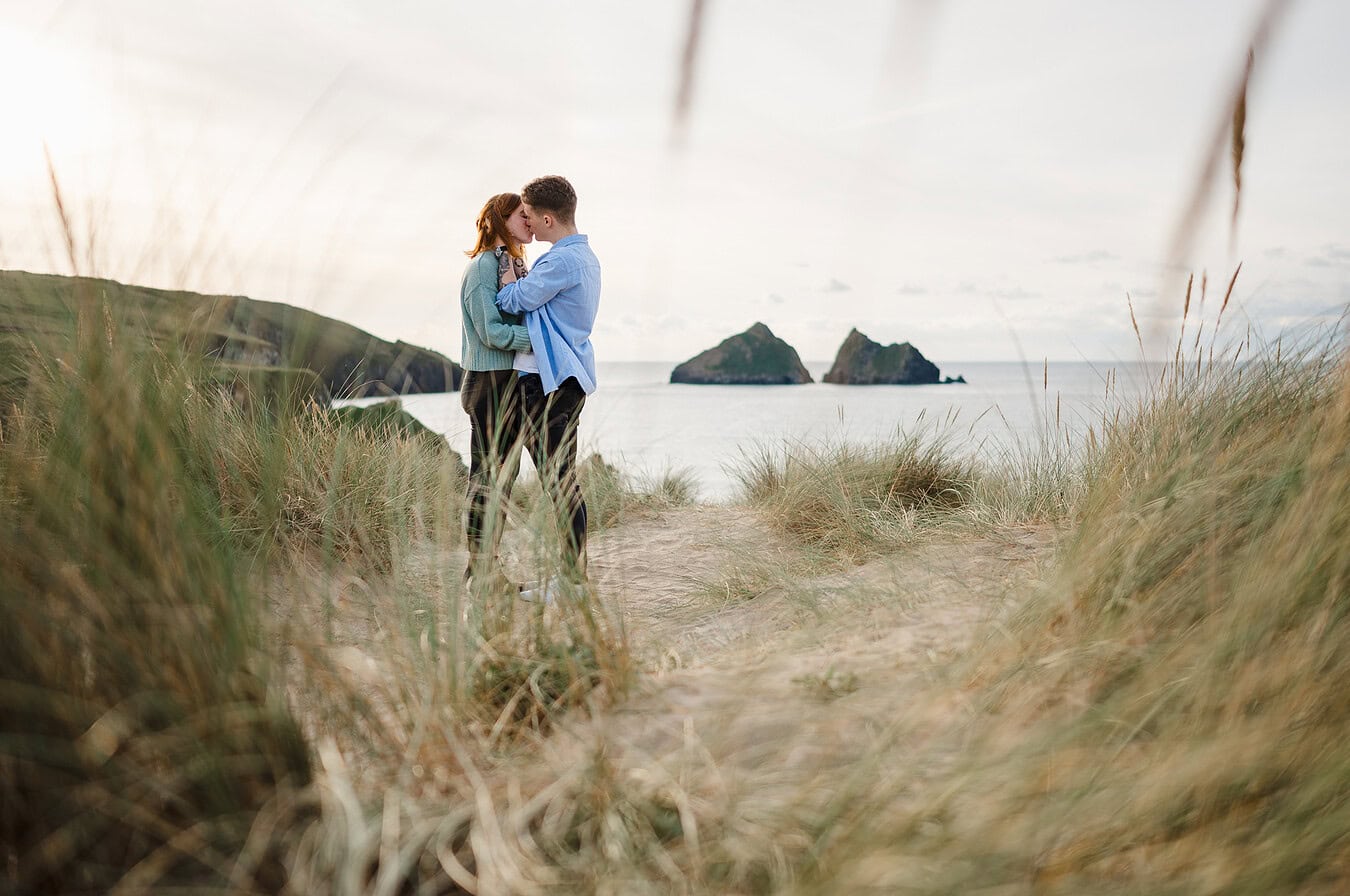 Through the dunes the happy couple kiss celebrating their engagement.