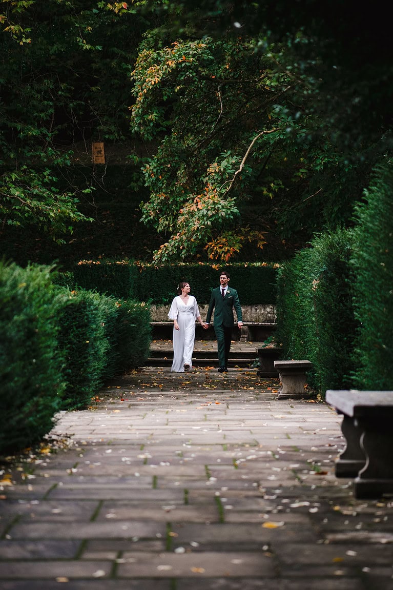 Bride and groom walking down the path through the green hedgerow