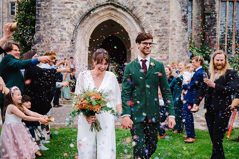 Happy couple walk through wedding confetti line - Writing The Perfect Modern Wedding Vows