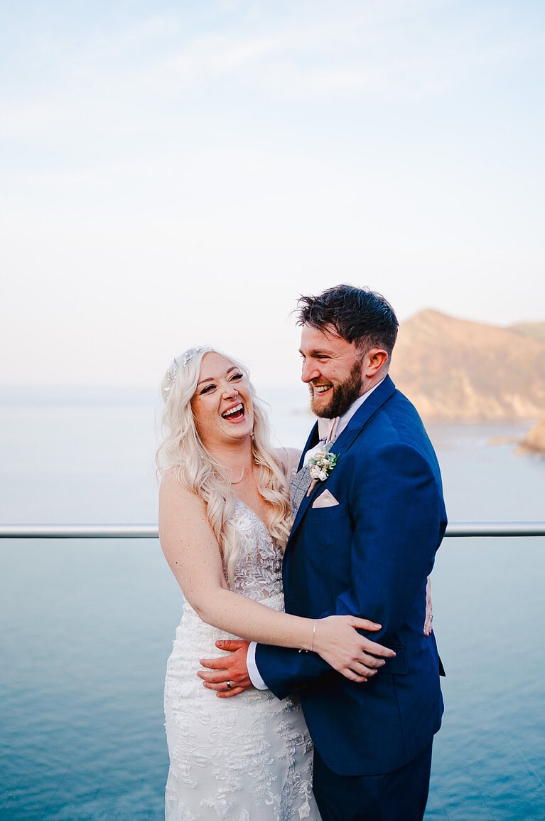 Wedding couple laughing on balcony overlooking the sea