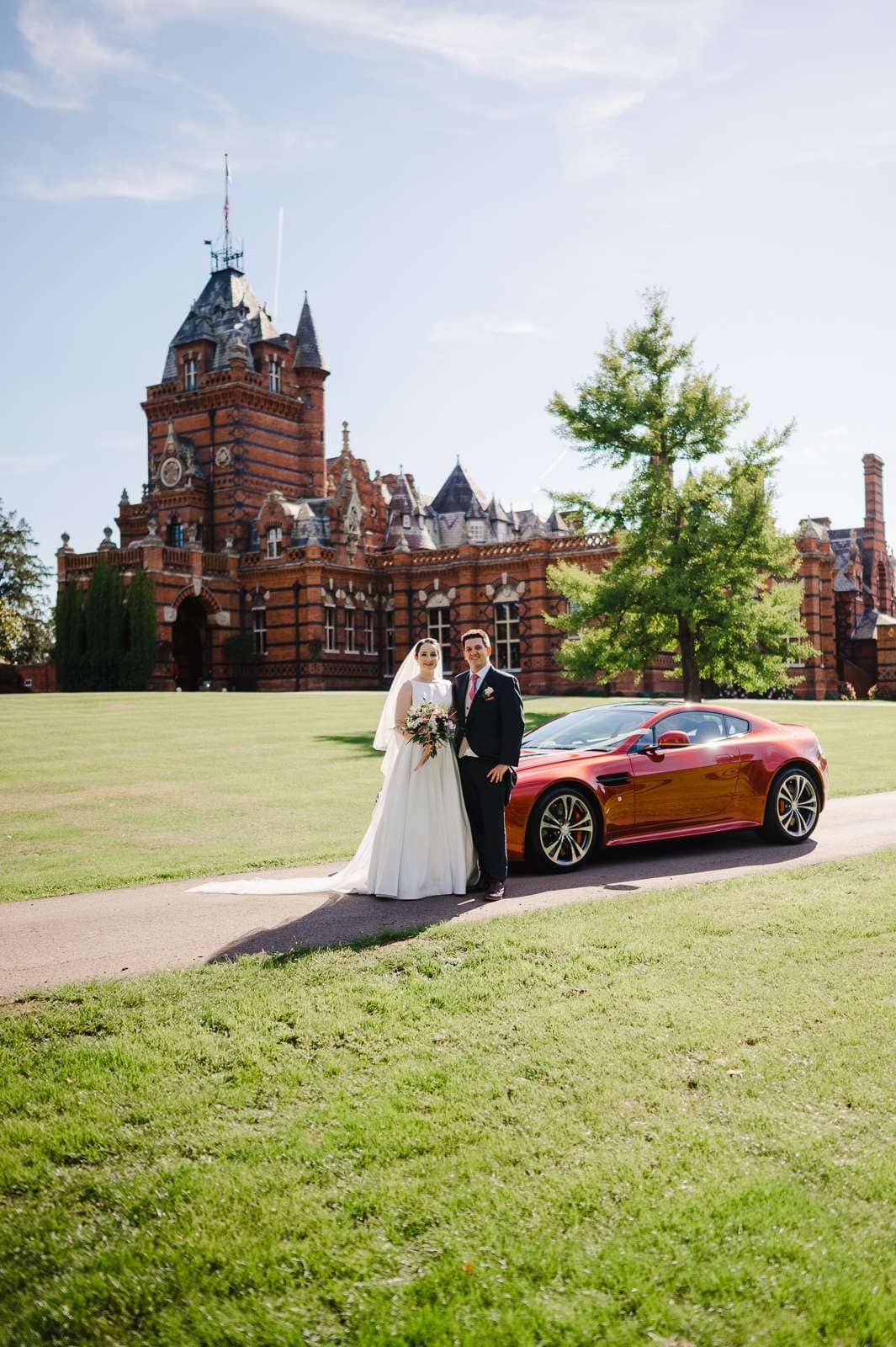 Couple happily pose besides their Jaguar and in front of their wedding venue - 7 Wedding Photos You Need To Put On Your Photography List