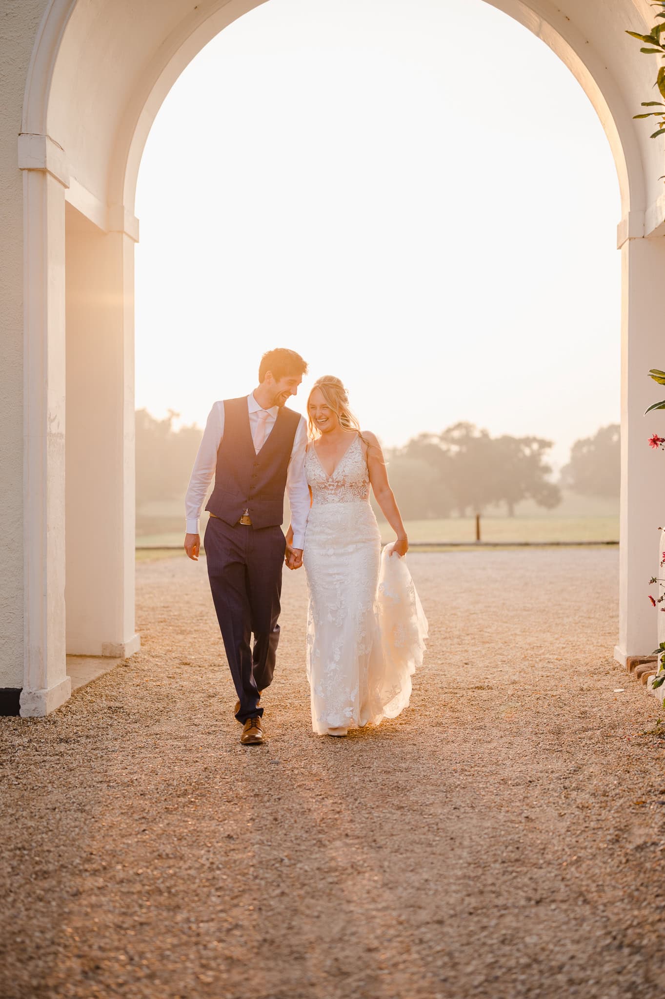 Wedding Couple walking through Rockbeare Manors archway as the golden sun sets. Taken by Jake Timms Photography - Devon Wedding Photographer
