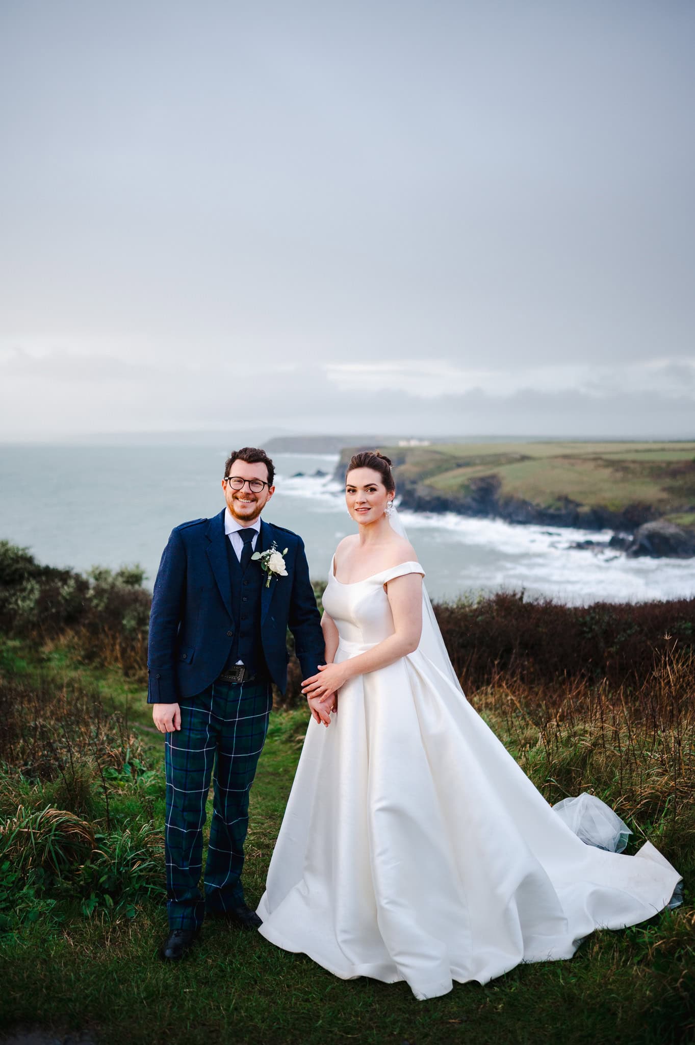 Happy newlyweds standalong the cliff tops outside Polurrian, photograph taken by Cornwall Weding Photographer, Jake Timms Photography
