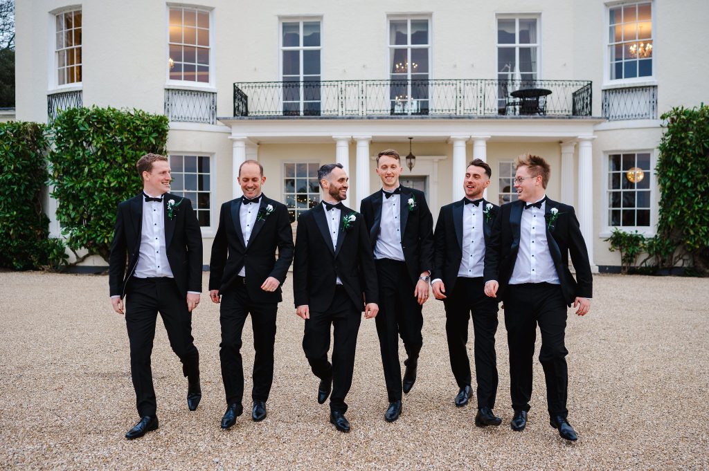 Grooms party walking with Rockbeare Manor in the bcakground