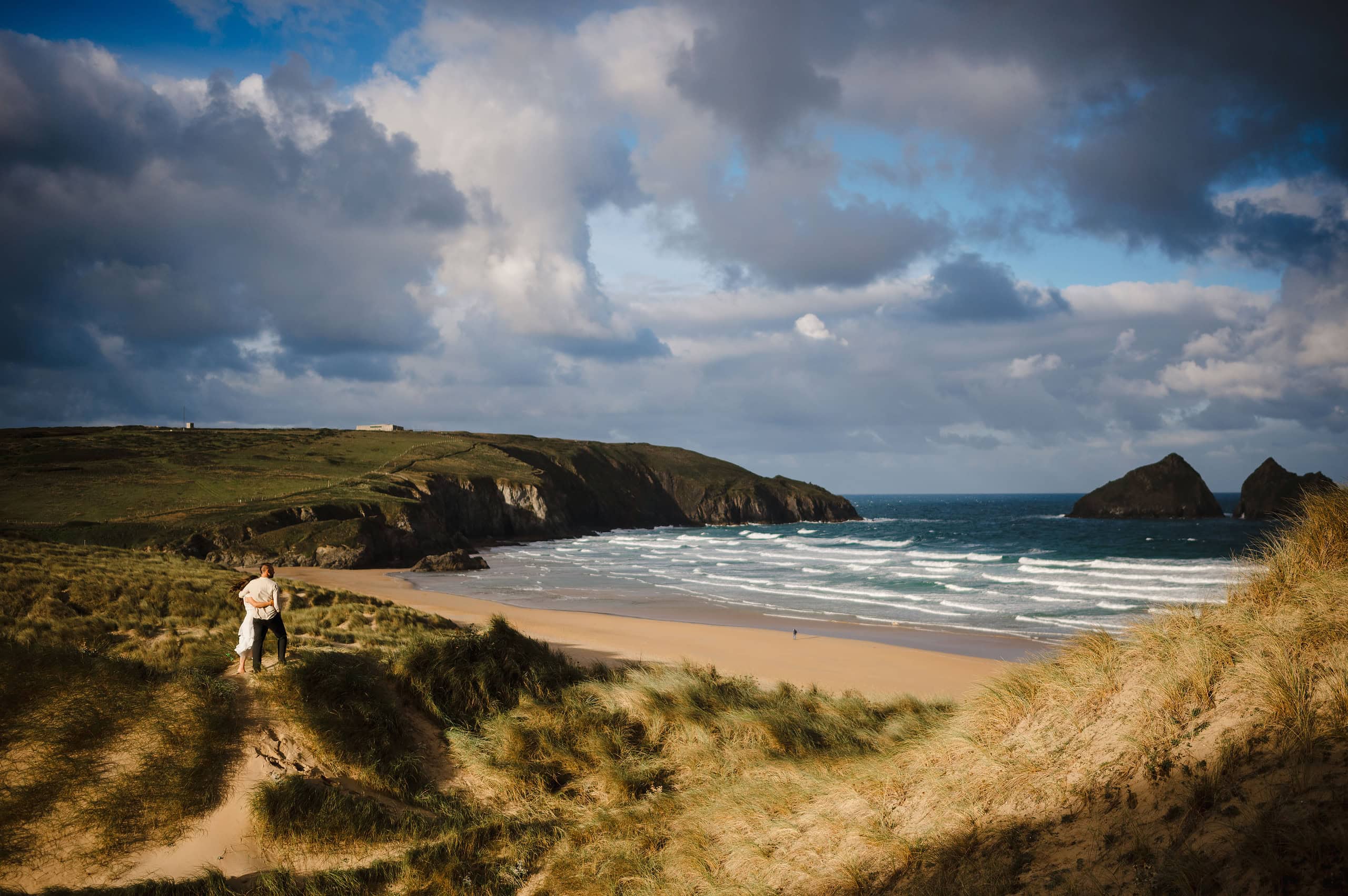 Standing above the golden bay as the sun rises and warms up the golden sand. Stunning Sunrise Elopement at Holywell Bay, Cornwall