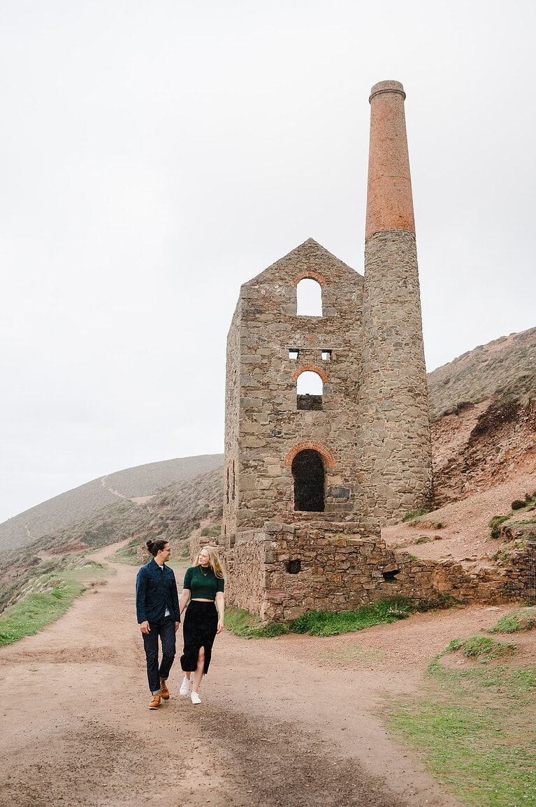 A huge mine in the background on a coast path in Cornwall as the couple walk by by Cornwall engagement photographer, Jake Timms Photography