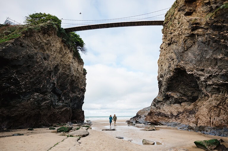 Walking underneath the bridge on Newquay beach during their Newquay engagement photoshoot