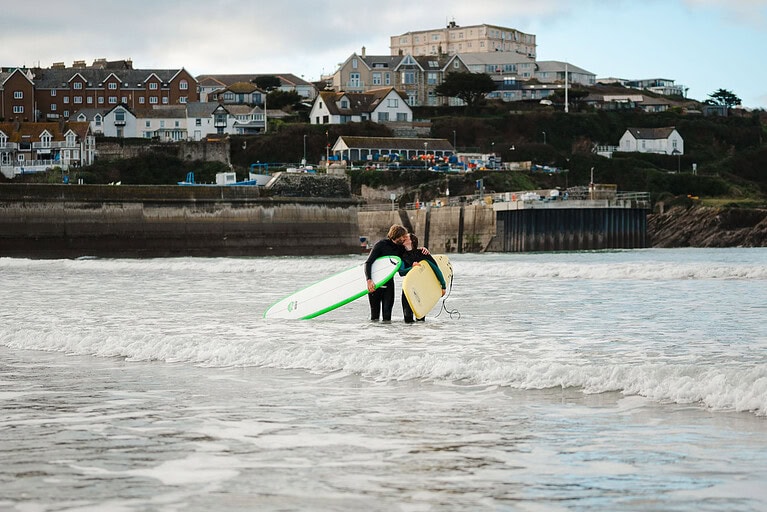 Getting out of the water as you take a kiss as you celebrate getting engaged during their Newquay engagement photo shoot by Cornwall engagement photographer