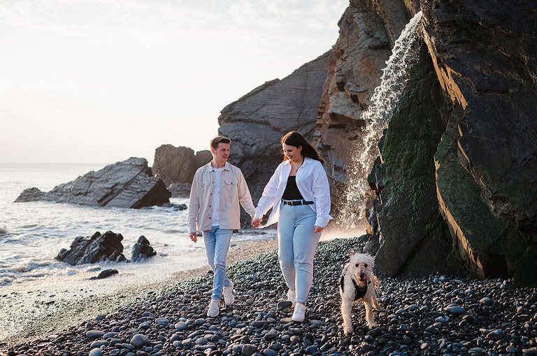 The couple walk along the rocky Sandmouth beach with their friendly dog by their side as the sun starts to set behind them