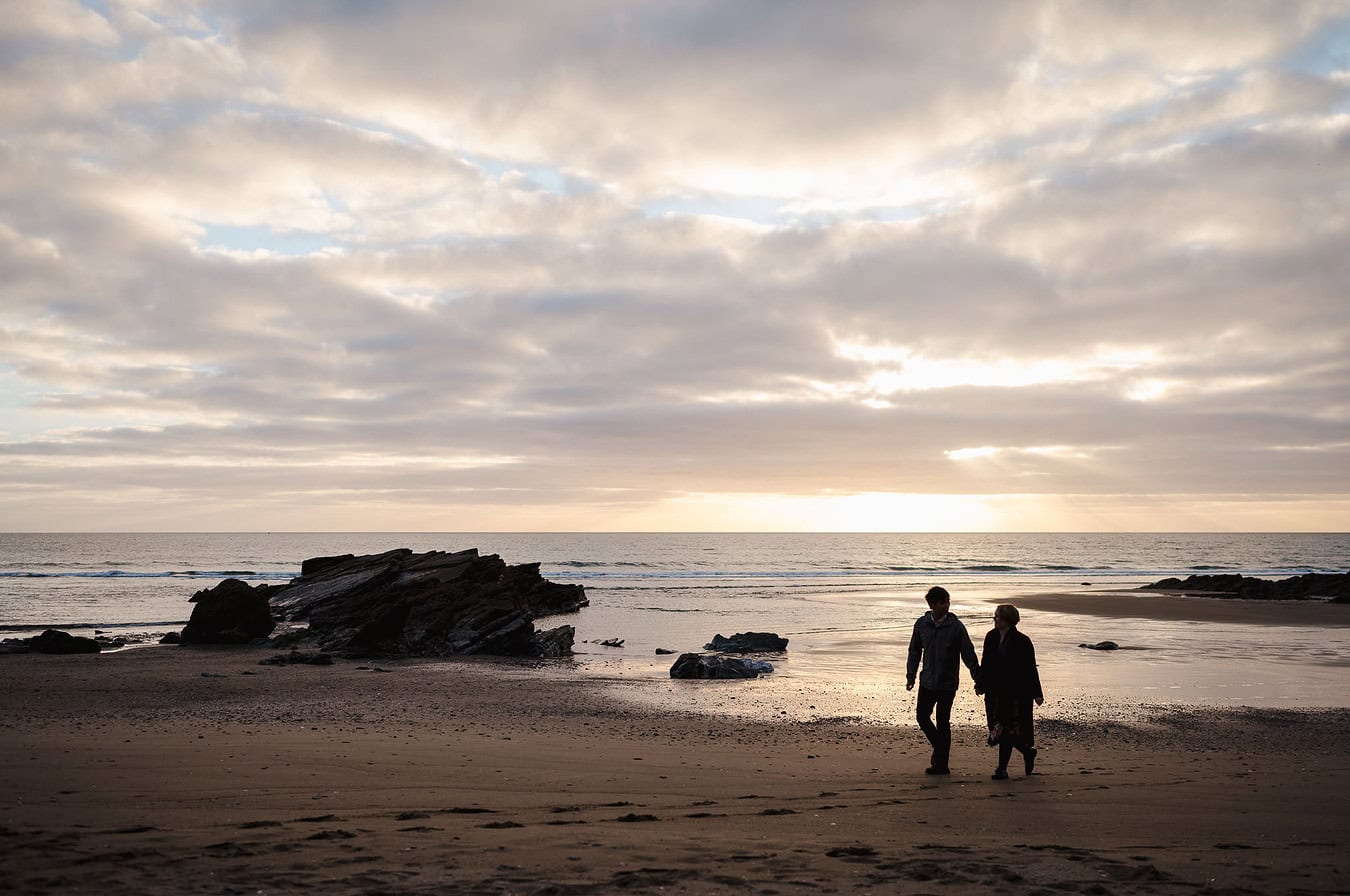 A silhouetted couple walking across the beach as the sunsets celebrates their engagement during their Whitsand Bay Engagement Photo Shoot