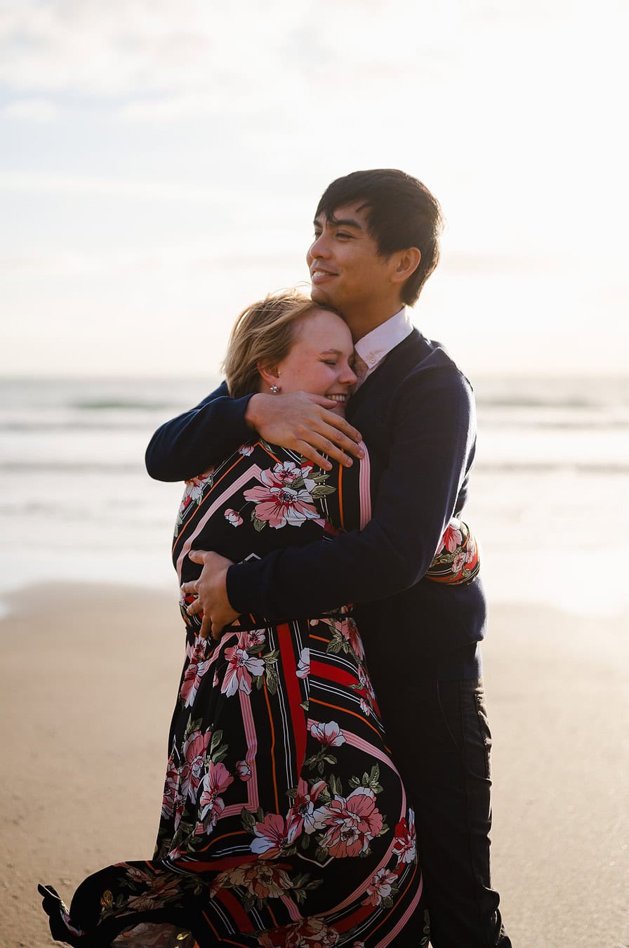 A laughing happy couple celebrate their Whitsand Bay engagement with a joyful hug by Cornwall Engagement photographer Jake Timms Photography