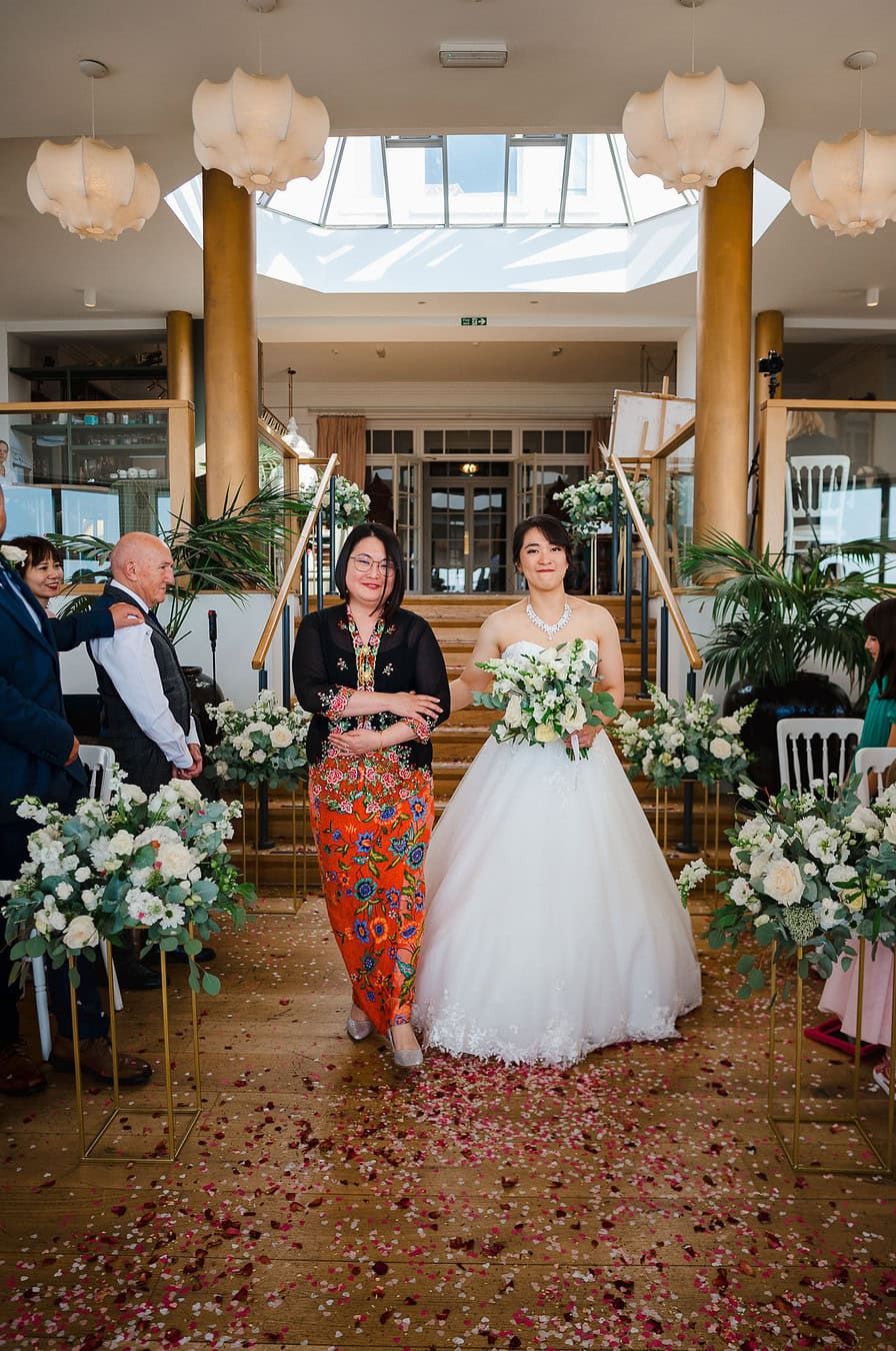 Bride walks over the flower-covered floor towards her partner at the end of the wedding aisle, photographed by Bath Wedding Photographer, Jake Timms Photography
