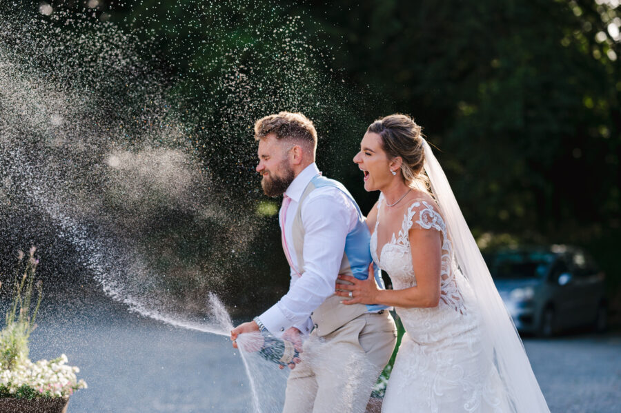 Wedding champagne spray in the face as the groom shakes the champagne bottle by Bath Wedding Photographer, Jake Timms Photography