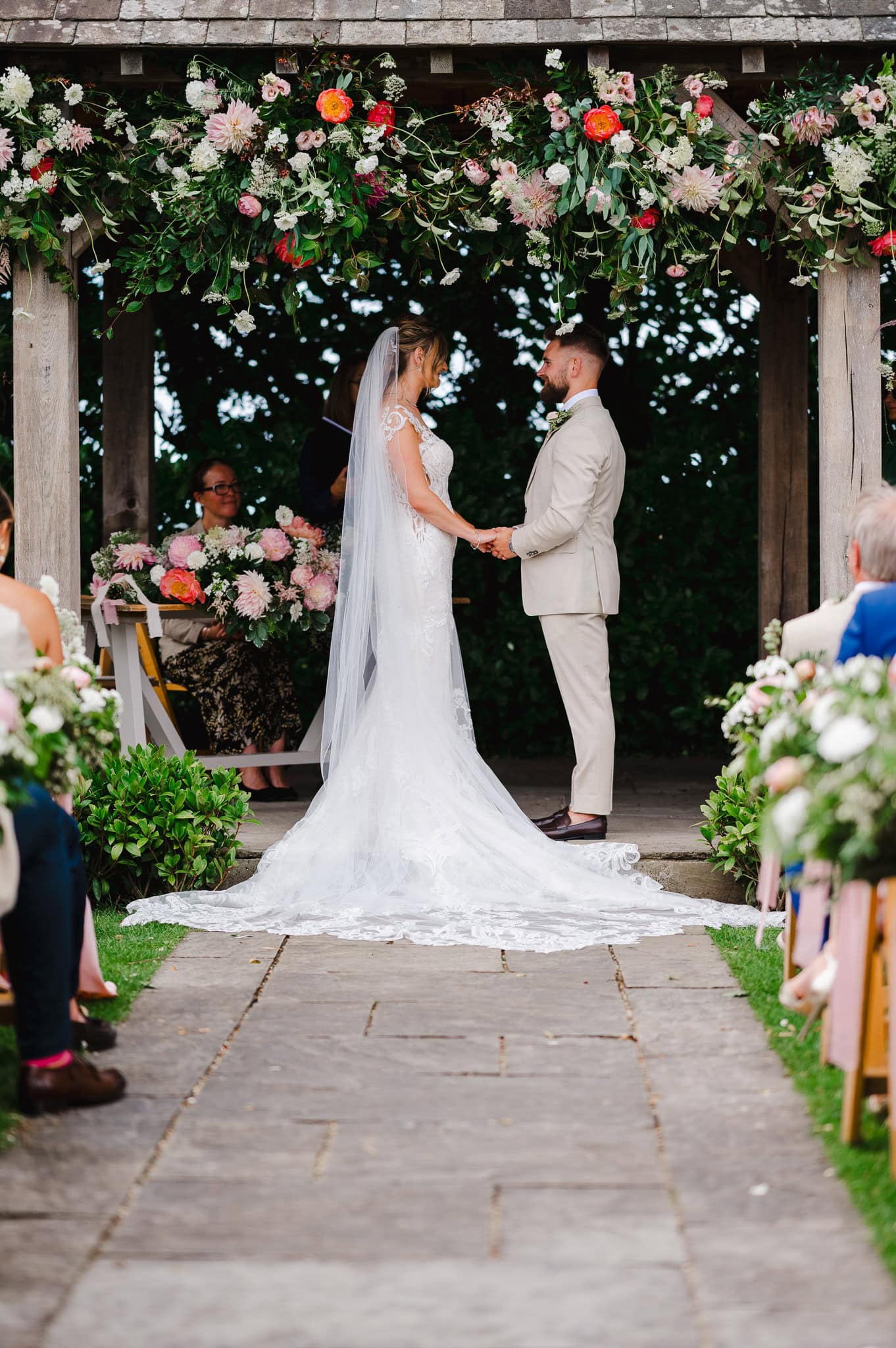 A wedding couple stands at the end of the wedding aisle underneath their beautiful flower archway by Exeter Wedding Photographer Jake Timms Photography