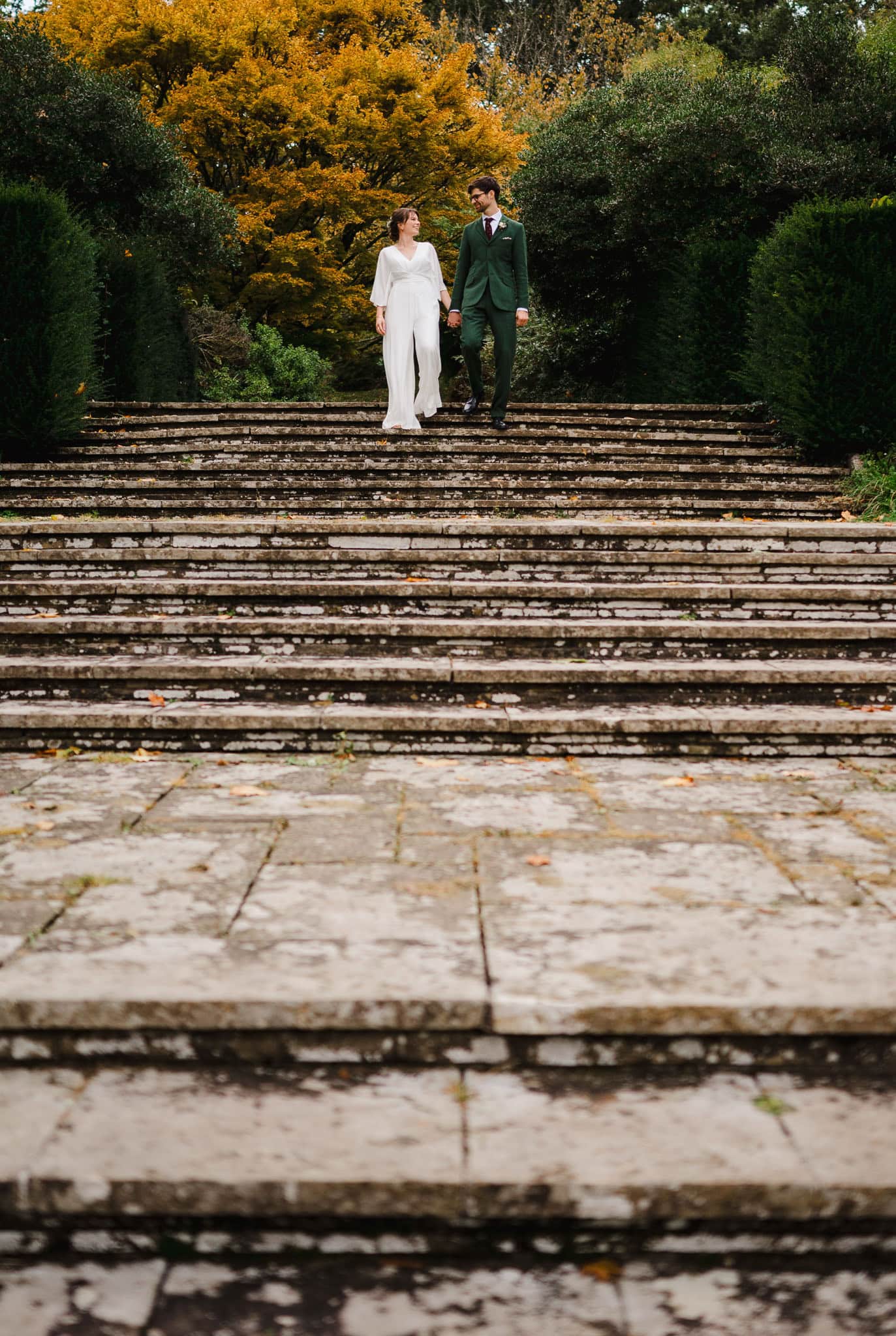 A wedding couple walks down the stone steps, surrounded by vibrant trees by Bristol Weding Photographer Jake Timms Photography