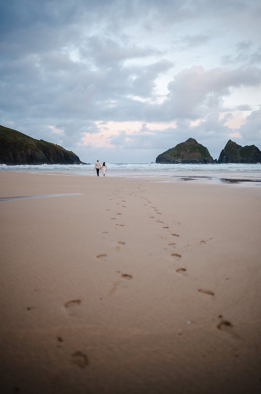 Walking across a sandy beach in Cornwall during their Cornwall Elopement - Elopement portfolio