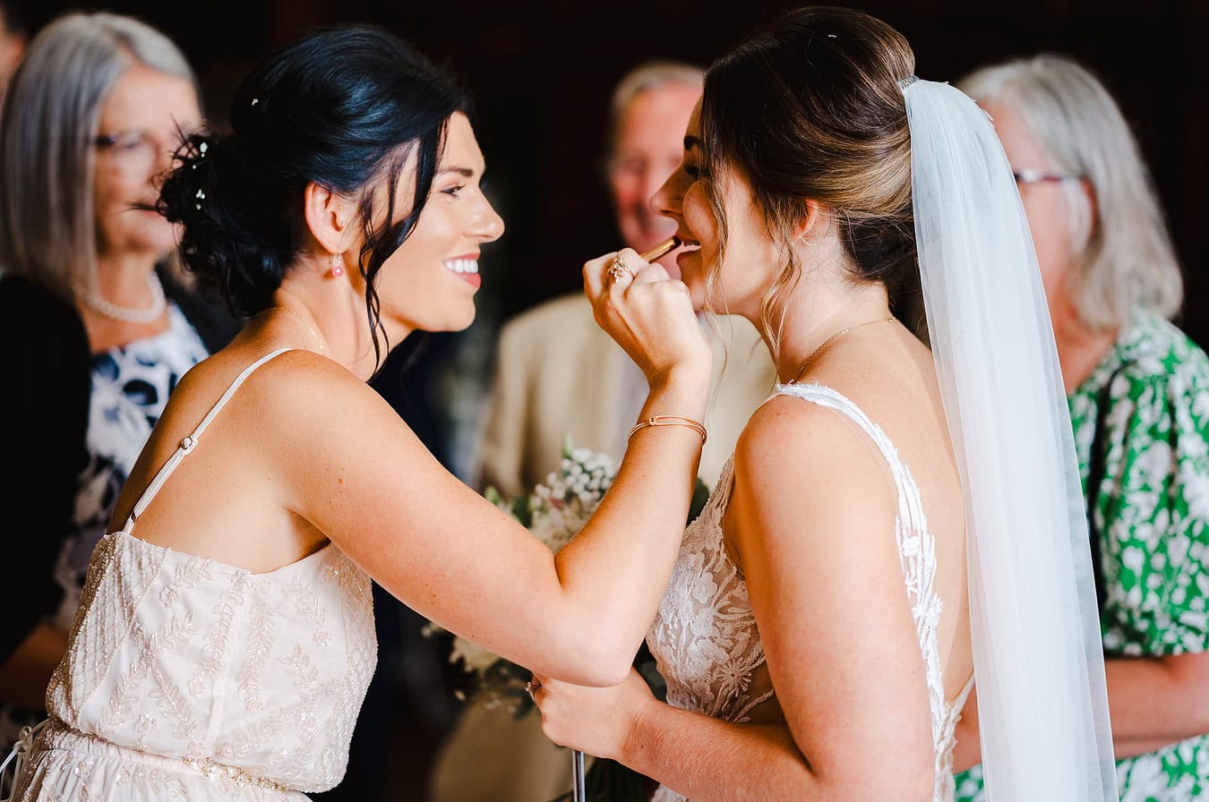 Maid of honour places lipstick on the bride