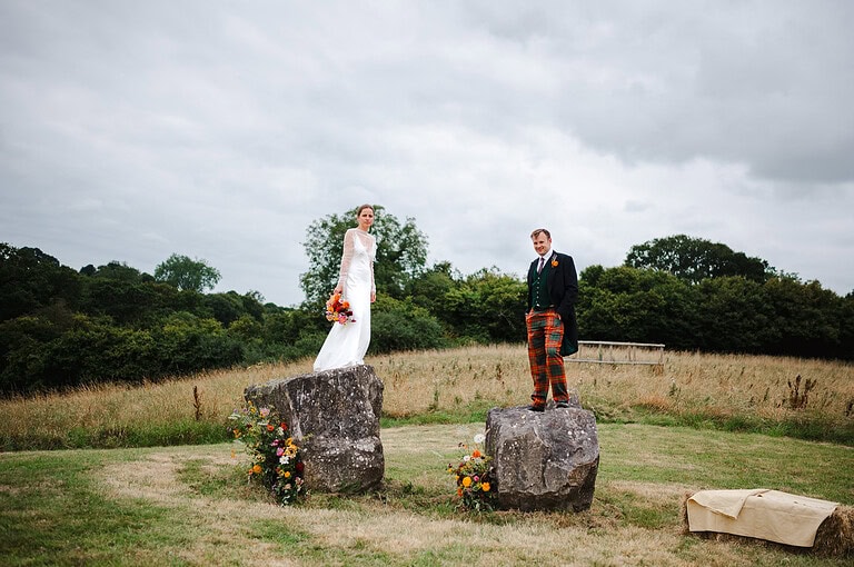 Jumping on top of two giant boulders as the couple look towards the camera for their portraits - Somerset Wedding
