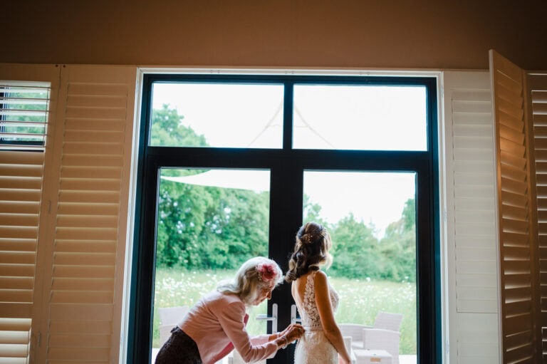 Mother of the bride fastens up the back of the wedding dress at Froginwell