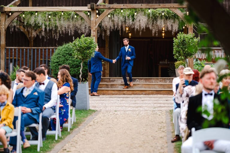 The groom starts to walk down his wedding aisle whilst shaking hands