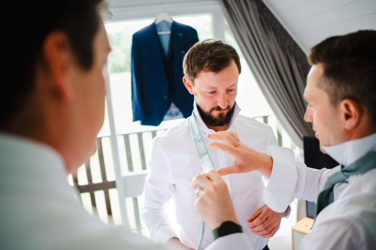 The groom is having help adjusting his tie by the groomsmen on his wedding day in Devon