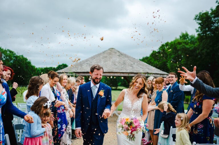 The happy couple laugh as wedding confetti is chucked over them at Froginwell. By Devon Wedding Photographer, Jake Timms Photography