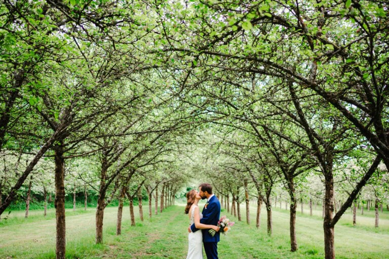 The happy couple share a kiss between the apple orchards at Froginwell by Devon wedding photographer, Jake Timms Photography