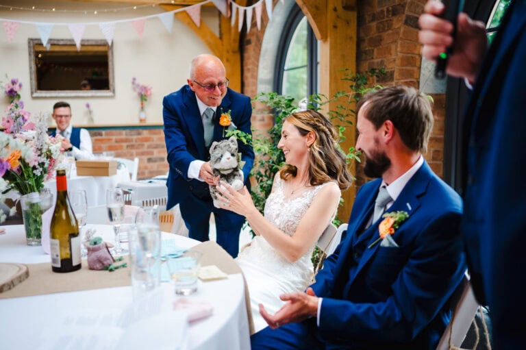 A joke from the dad as he passes over the stuffed cat to the newlyweds