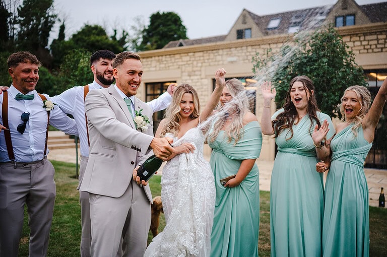 Shaking a bottle of champagne and let it spray to celebrate getting married at The Pear Tree Purton By Jake Timms Photography