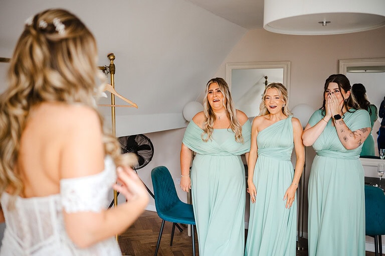 The bride shows off her wedding dress to her bridesmaids to as they look in shock and excitement