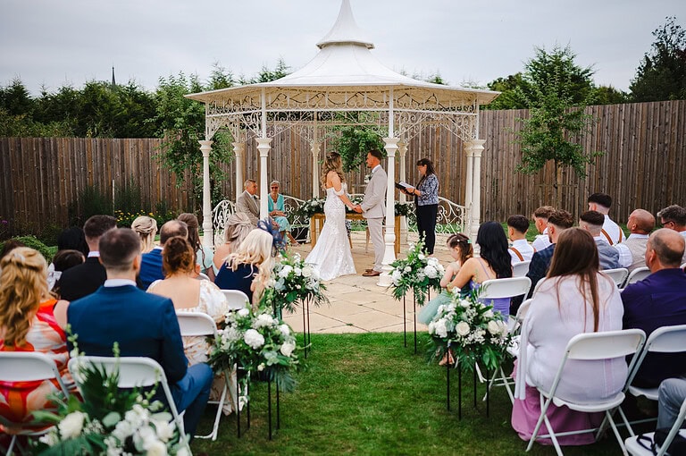 Bride and groom, hand in hand looking into each others eyes at the end of the aisle at The Pear Tree Wedding Venue