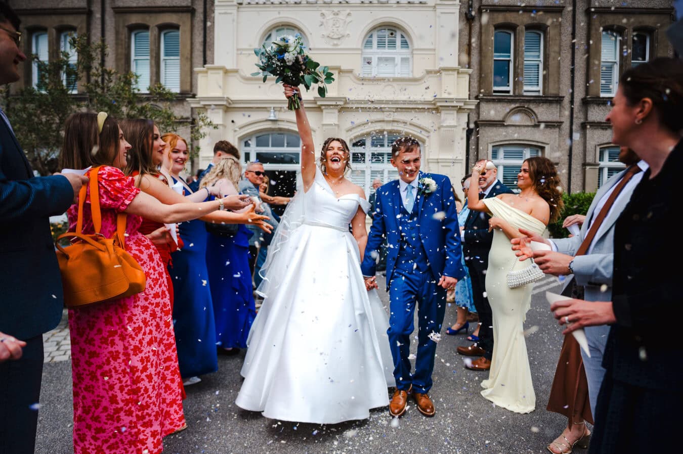 Throwing the wedding bouquet into the air as the happy couple celebrate whilst walking down the confetti aisle in front of the entrance to the Harbour Hotel Padstow By Cornwall Wedding Photographer, Jake Timms Photography