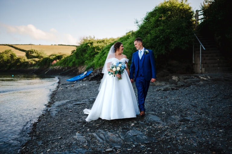 Happy couple walk along a secluded beach along the Camel Estuary in Cornwall for couple portraits