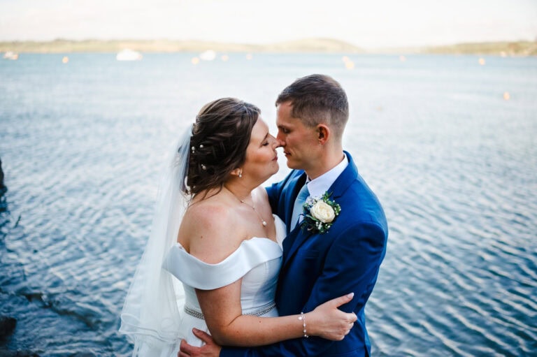 The happy couple go in for a kiss during their couple portraits set amongst the beautiful blue sea of Cornwall. By Cornwall Wedding Photographer, Jake Timms Photography